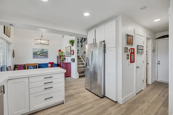 Open-concept interior featuring light wood-finish flooring, white cabinetry, a stainless steel refrigerator, recessed lighting, and a modern rectangular chandelier