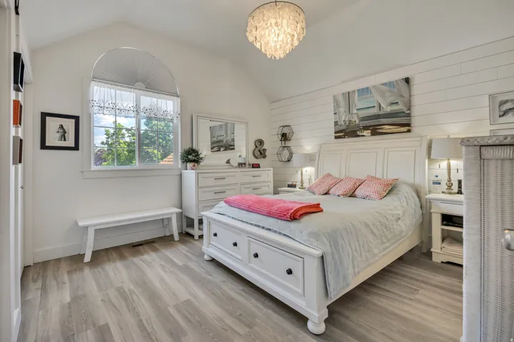 Vaulted ceiling bedroom featuring wood-finish flooring, a decorative chandelier, and an arched window
