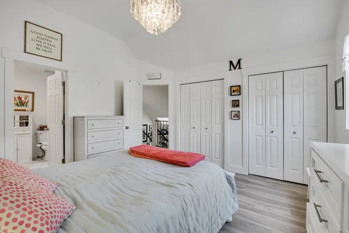 Vaulted ceiling bedroom featuring wood-finish flooring, a contemporary chandelier, and two sets of white bi-fold closet doors