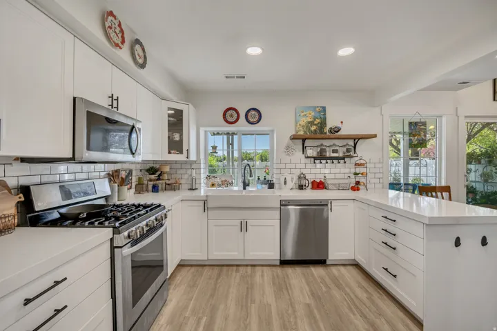 Modern kitchen featuring stainless steel appliances, white cabinetry with dark hardware, white subway tile backsplash, white countertops, and wood-finish flooring