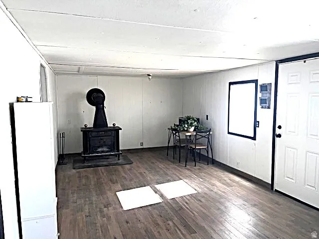 Spacious room featuring wood-finish flooring, a prominent cast iron stove with a stovepipe, and white paneled walls