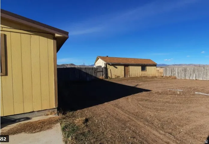 Spacious outdoor area featuring a separate utility building with a door and window, perimeter fencing, and a vast expanse of open ground