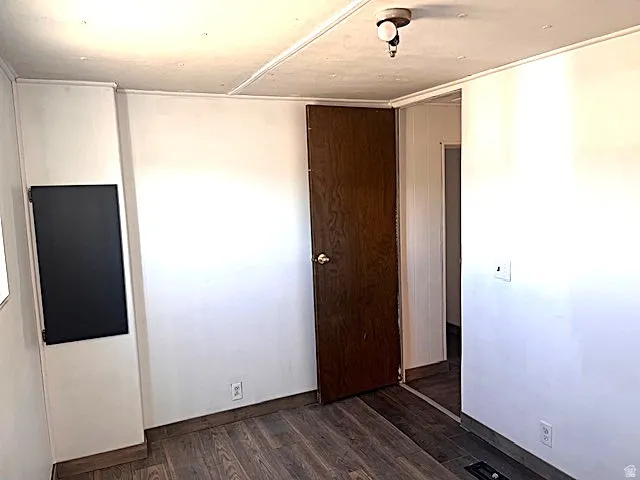 Room featuring wood-finish flooring, white walls, and a dark wood-finish door