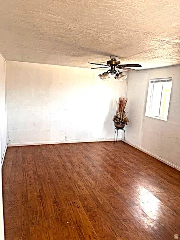 Spacious room featuring wood-finish flooring, a multi-speed ceiling fan with integrated lighting, textured white walls, and a window for natural light
