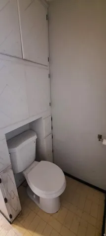 Bathroom featuring a white toilet, integrated cabinetry with geometric paneling, and checkerboard floor tiling