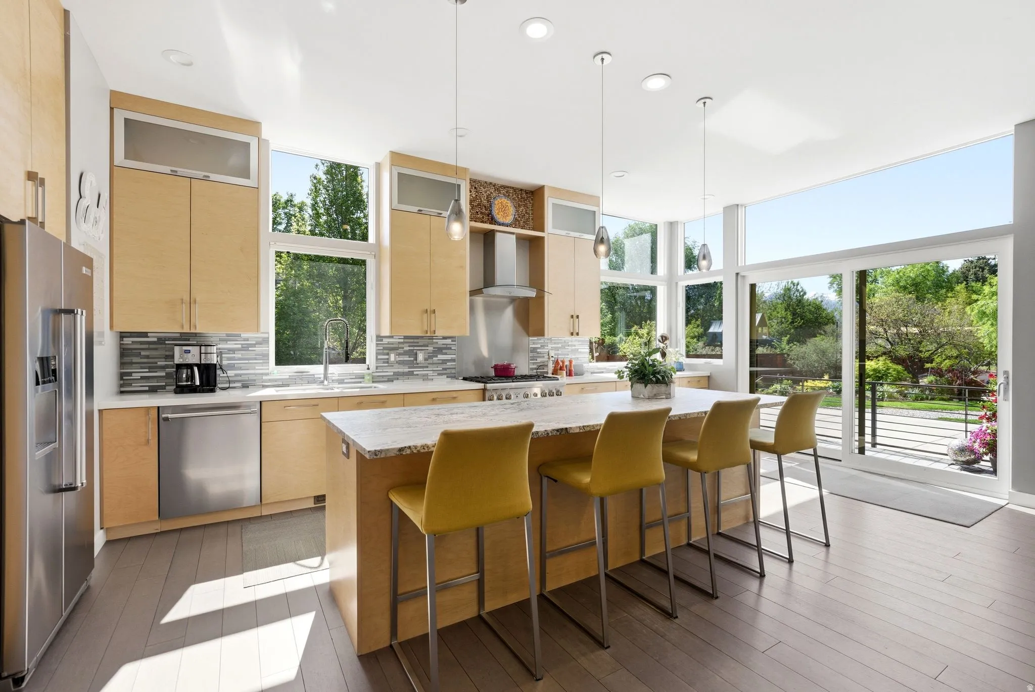 Expansive kitchen featuring light wood cabinetry, a large center island with a light-toned countertop, stainless steel appliances, and wood-finish flooring