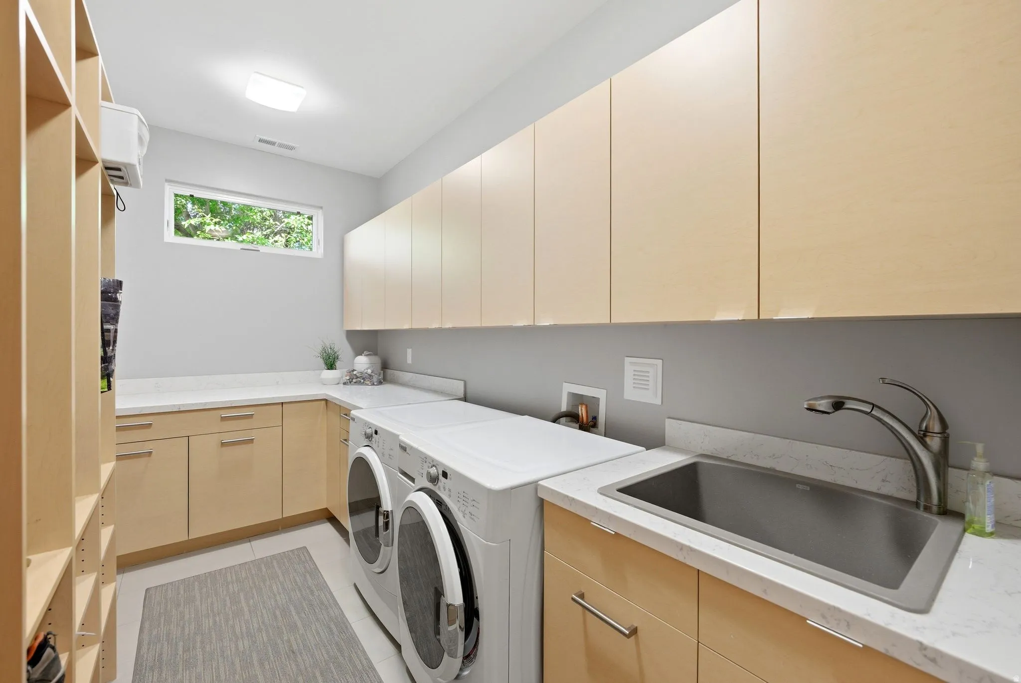 Laundry room with light wood-finish cabinetry, white countertop surfaces, and a stainless steel utility sink with a gooseneck faucet