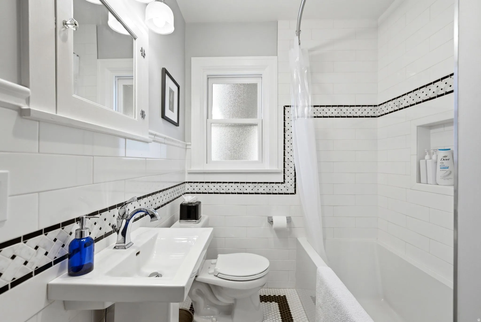 Bathroom featuring white subway tile walls with black accent banding, a pedestal sink with chrome faucet, a toilet, and a bathtub with an integrated shower niche