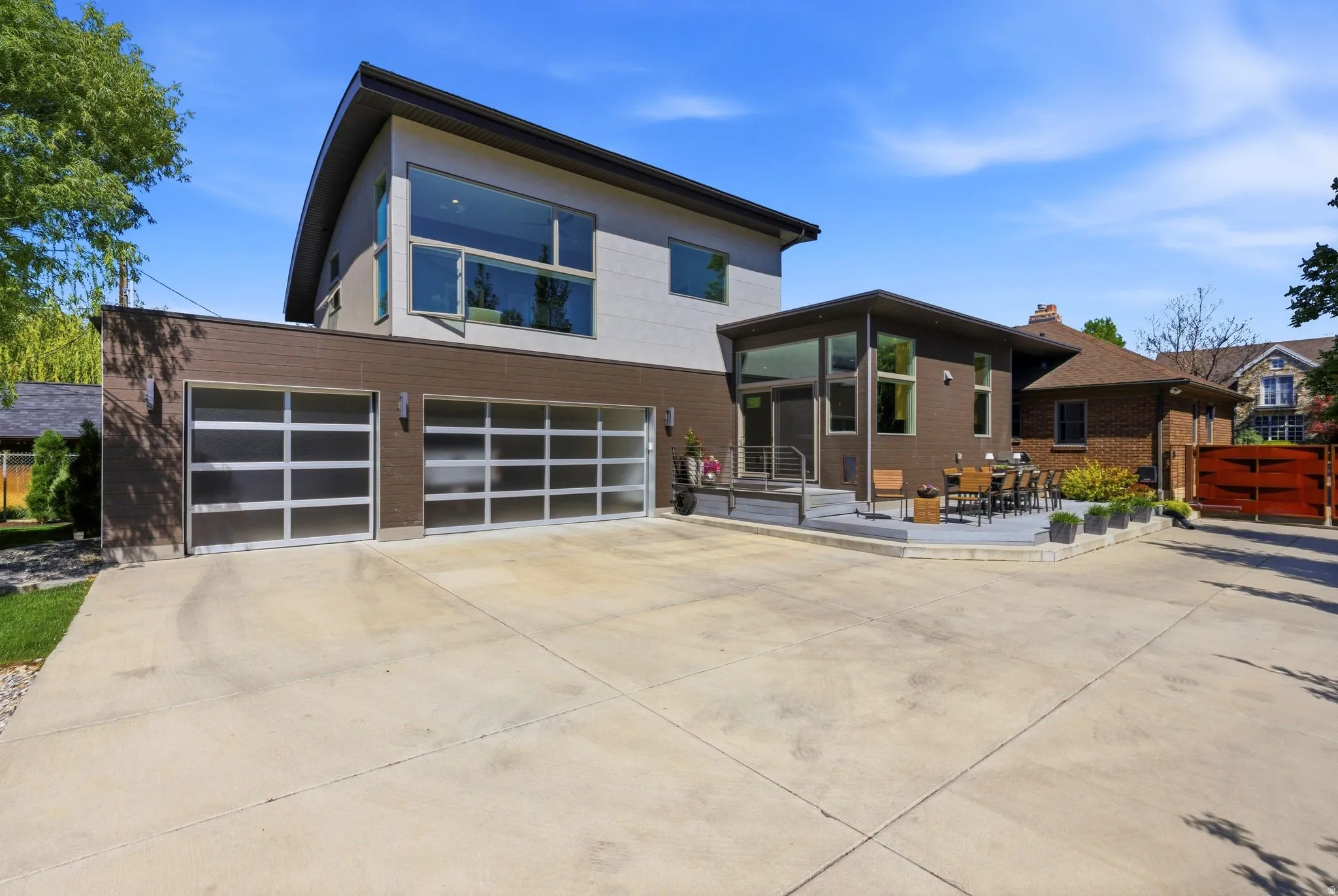 Contemporary architectural design featuring a two-car garage with frosted glass doors, a large concrete driveway, and a tiered outdoor patio