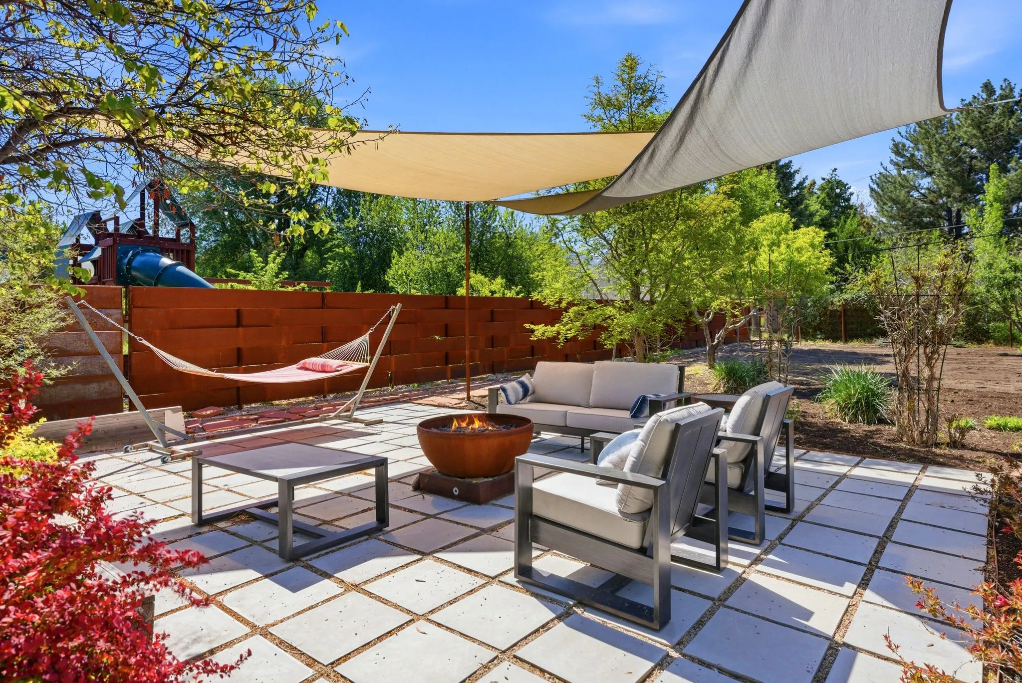 Spacious outdoor patio featuring large square pavers, dual sun shades, and a built-in fire pit