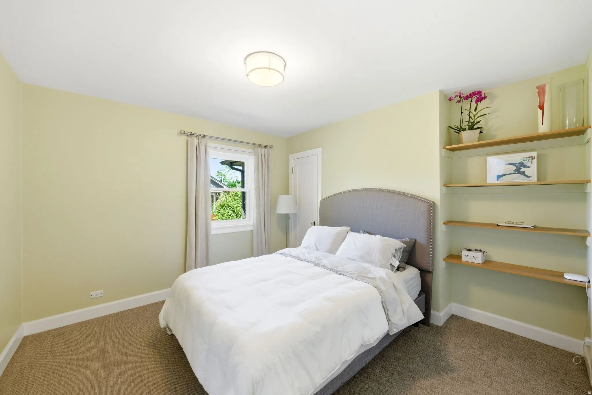 Bedroom featuring a neutral color palette, built-in shelving, sconce lighting, and a window with white trim