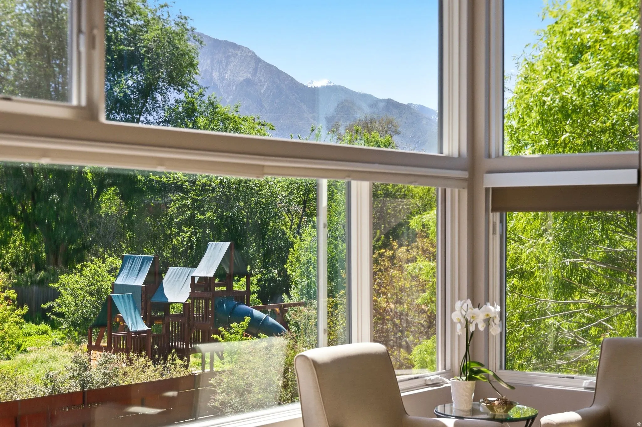 Floor-to-ceiling windows with roller shades, overlooking lush green trees and distant mountains