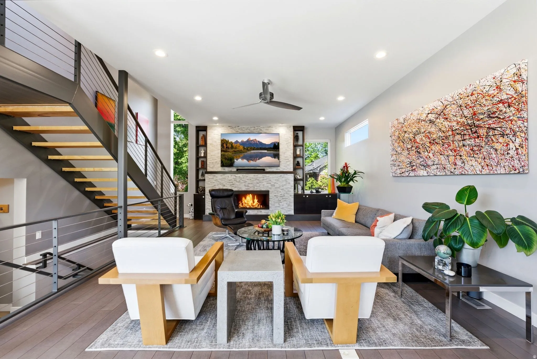 Open-concept living area featuring wood-finish flooring, a contemporary fireplace with a stacked stone surround, and recessed lighting