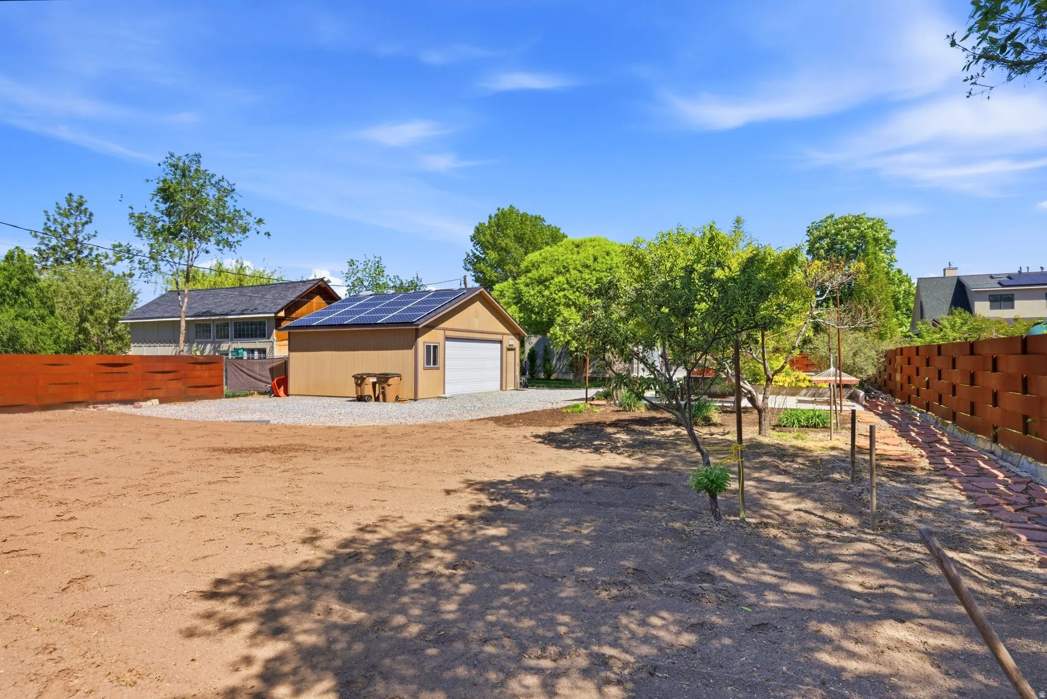 Detached garage with solar panels, a gravel parking area, and a large cleared lot