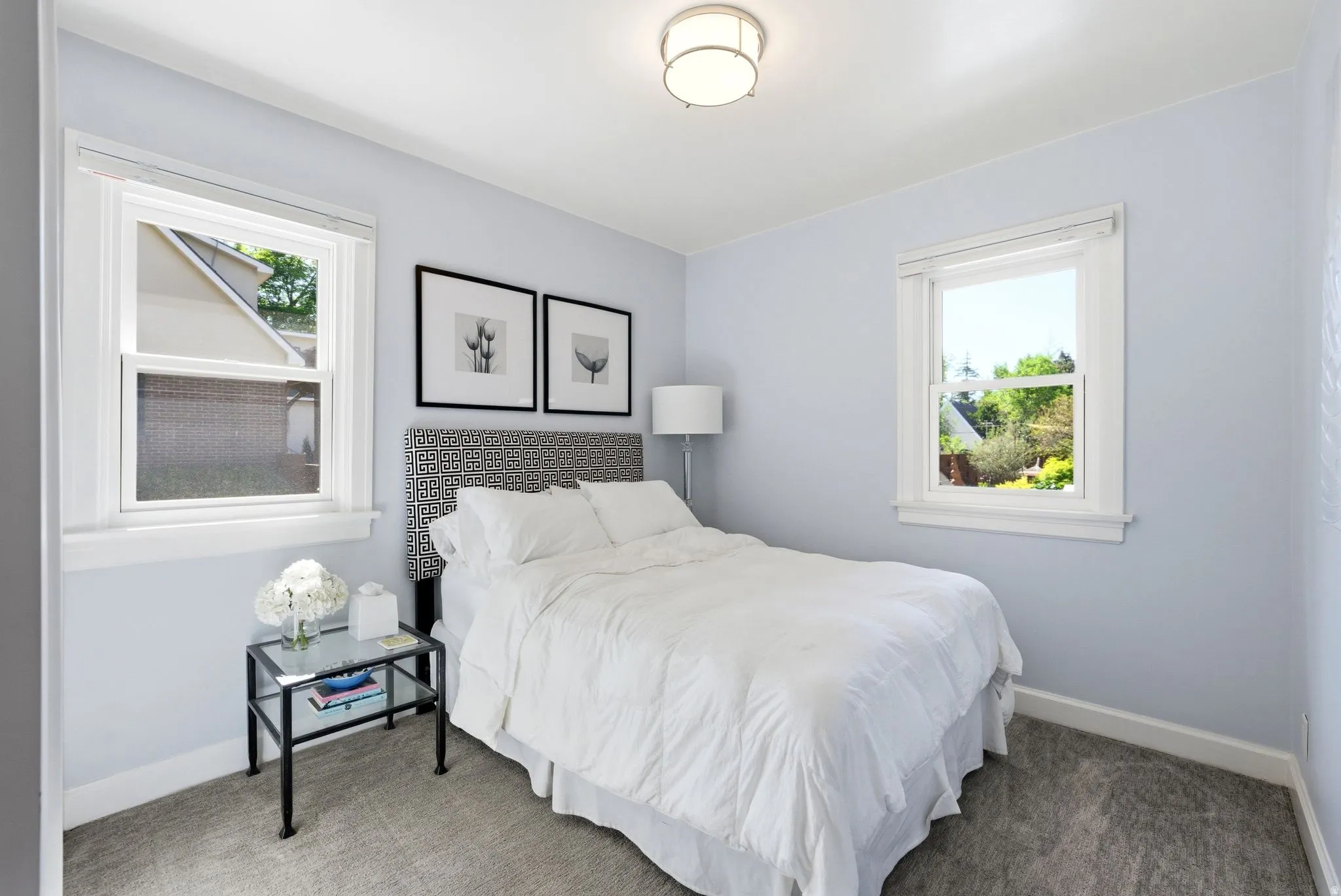 Bedroom featuring two single-hung windows with white trim, light blue walls, and a flush mount ceiling light