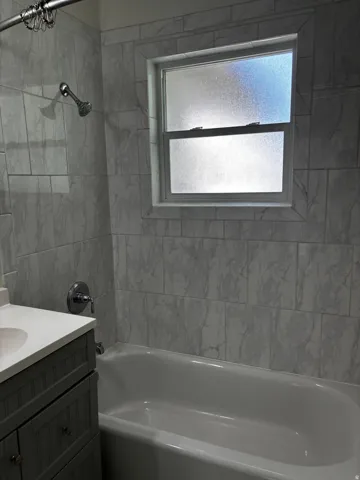 Bathroom featuring a white bathtub, light-toned tile surround, and a frosted window