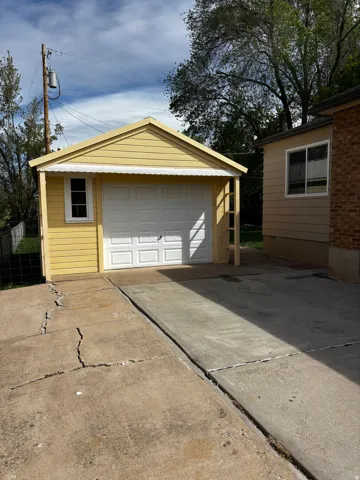 Detached single-car garage with a white panel door and a side window, featuring yellow siding and a gabled roofline