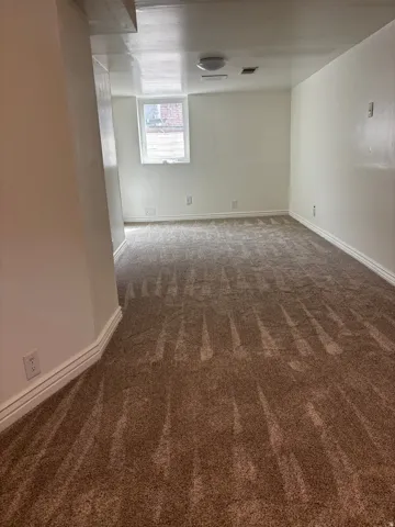 Spacious room featuring new brown carpet, white baseboards, and a single window