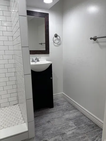Bathroom featuring a black vanity with an integrated white sink, a framed mirror, and a white subway tile shower with a hexagonal tile floor