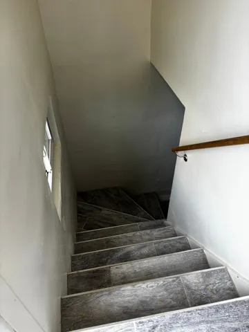 Staircase featuring wood-look tile treads and risers, a natural wood handrail, and a small window for ambient light