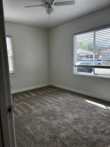 Room featuring plush gray carpet, white walls, and a ceiling fan with integrated lighting