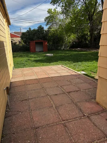 Expansive backyard featuring a red paver patio, established lawn, mature trees, and a metal storage shed