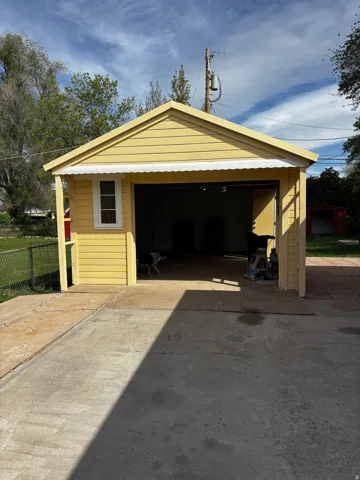 Detached garage featuring yellow siding, a white window, and a corrugated metal awning