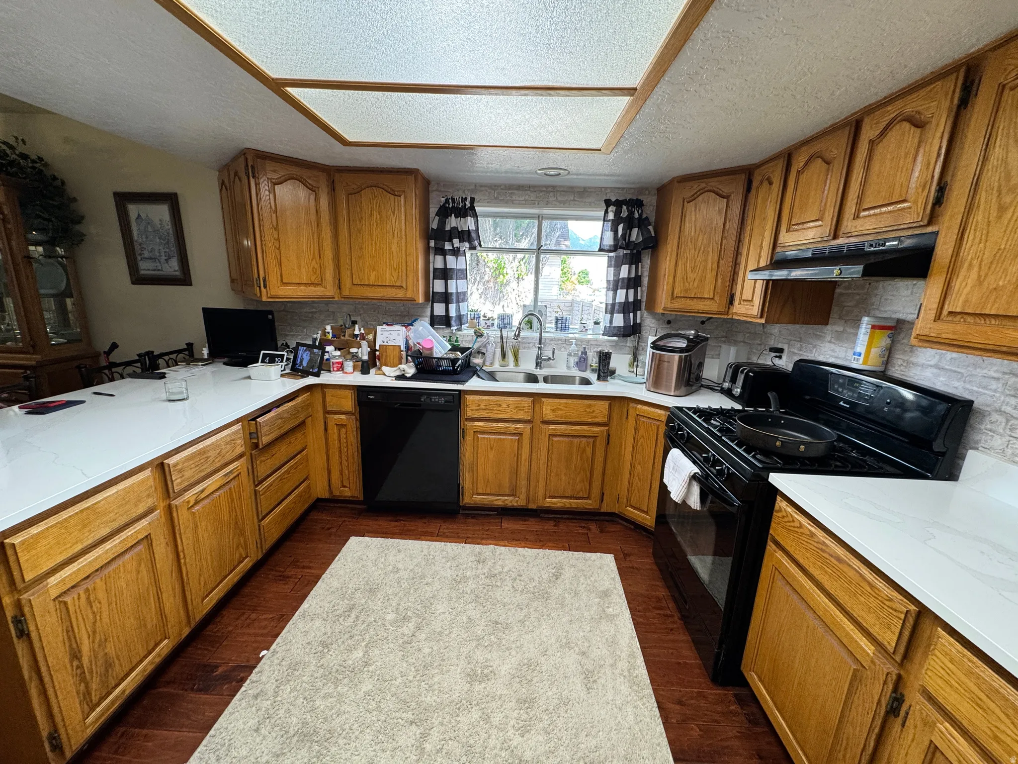 Kitchen featuring expansive white countertops, wood cabinetry, built-in dishwasher, gas range, and wood-finish flooring