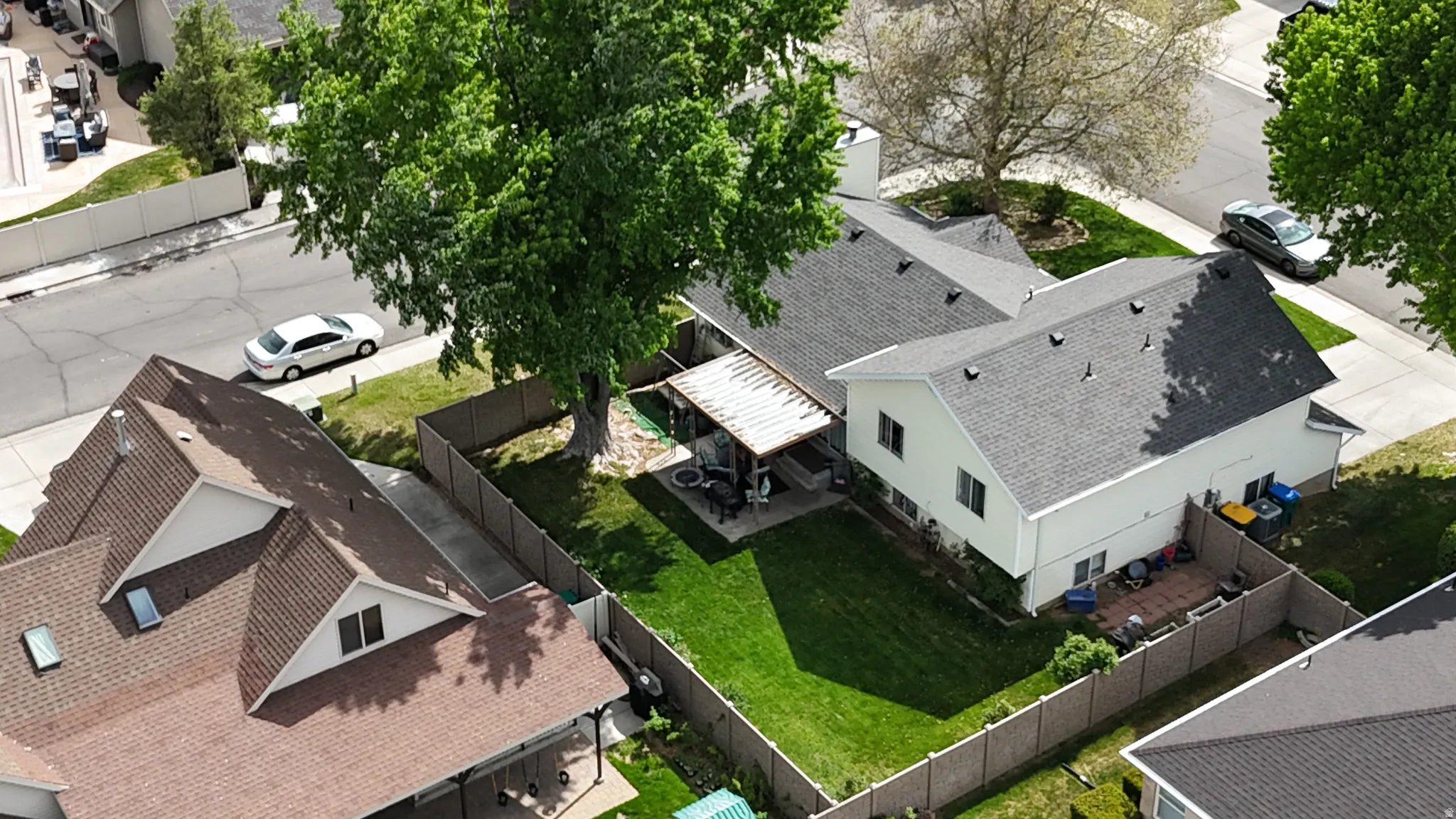 Expansive fenced backyard featuring a manicured lawn, mature trees, and a covered patio area