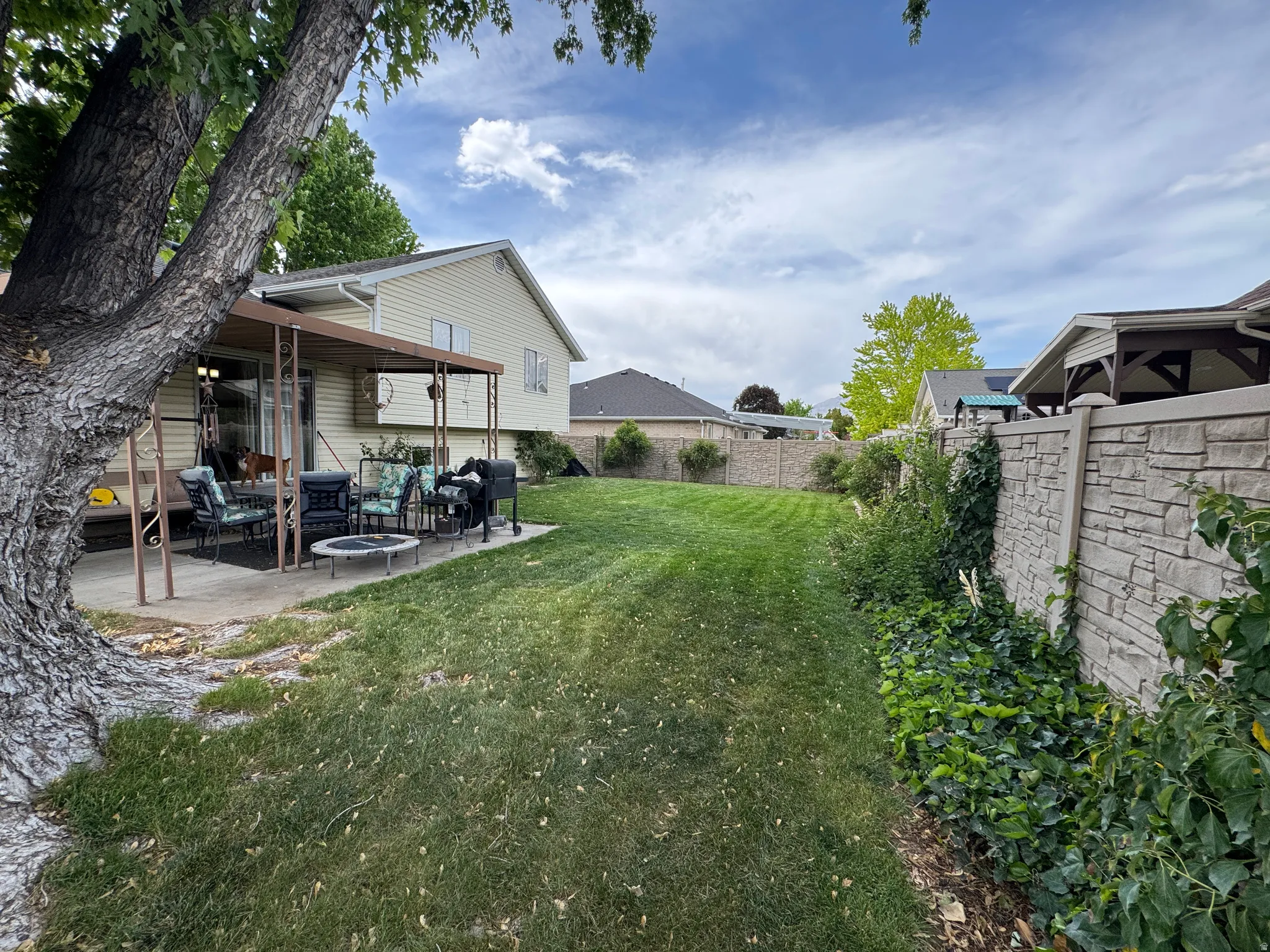 Expansive backyard featuring a lush lawn, mature perimeter landscaping, and a stone-style privacy fence