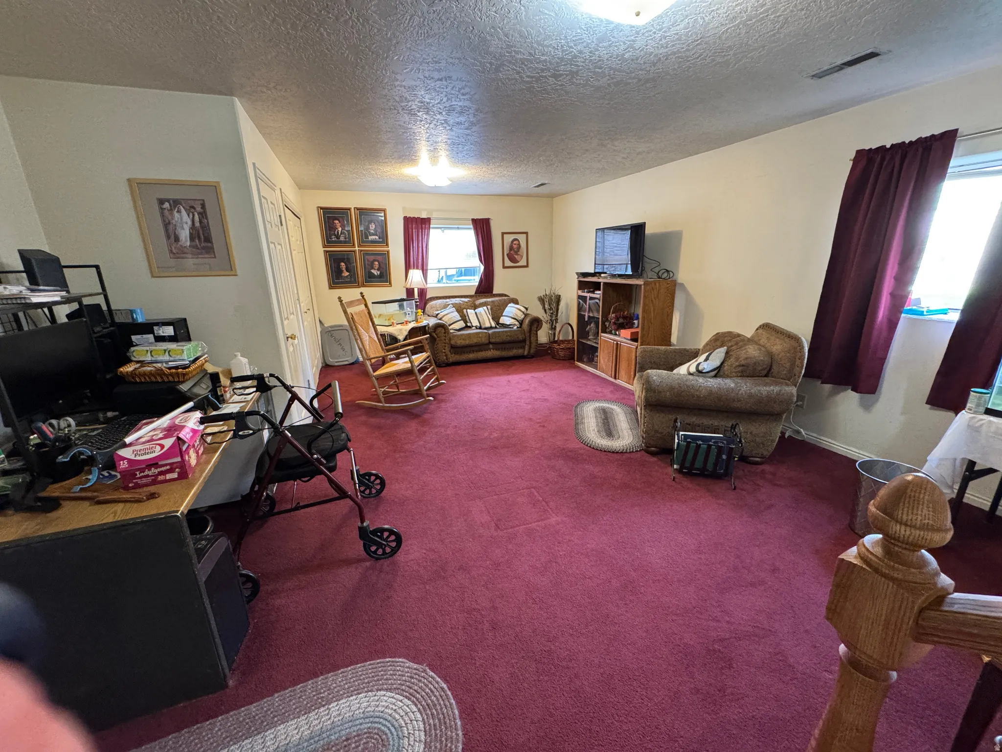 Spacious room featuring plush red carpeting, light-colored walls, and multiple windows with drapery