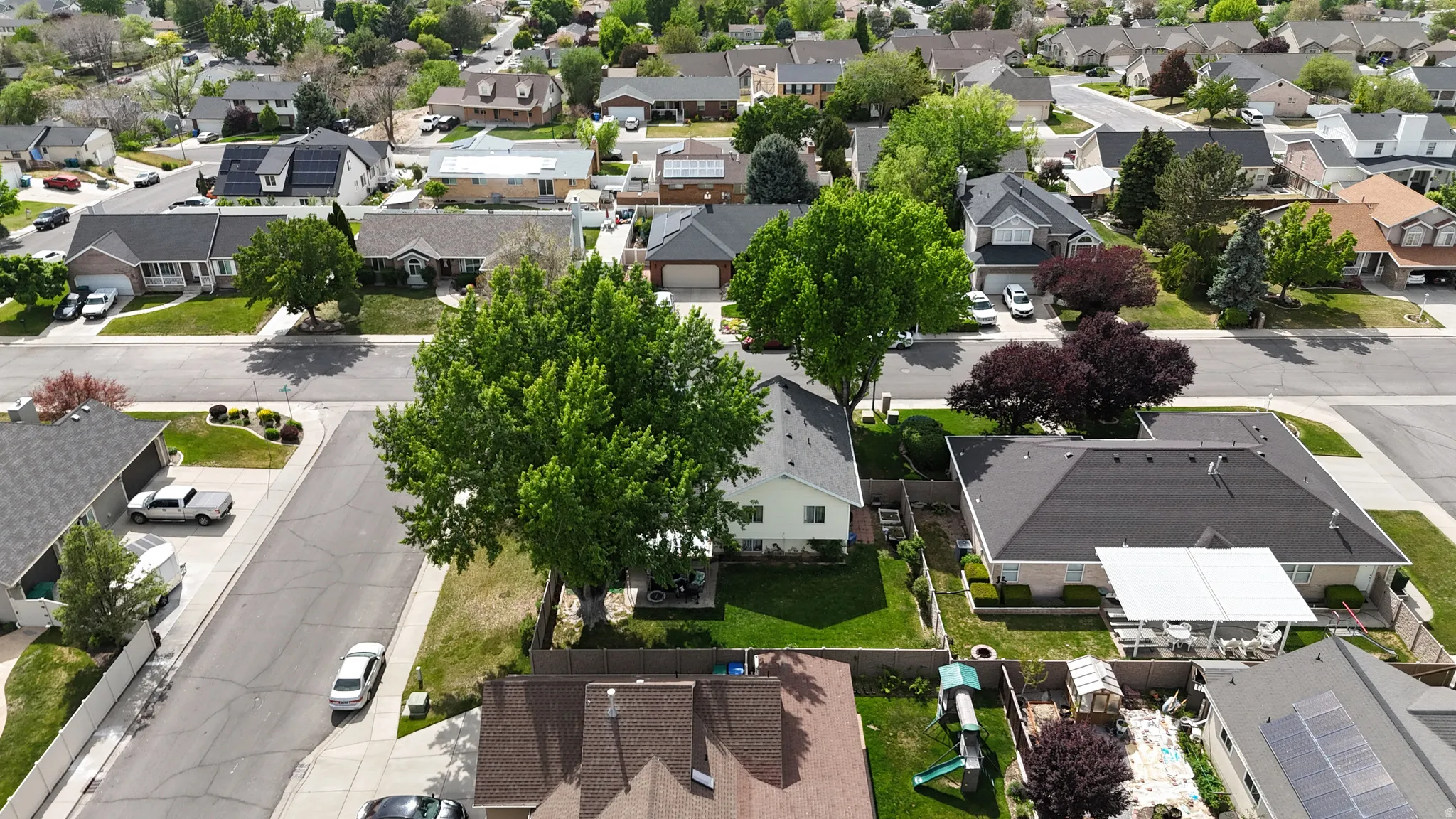 Spacious residential property with a dark shingle roof, established landscaping, and a covered patio structure