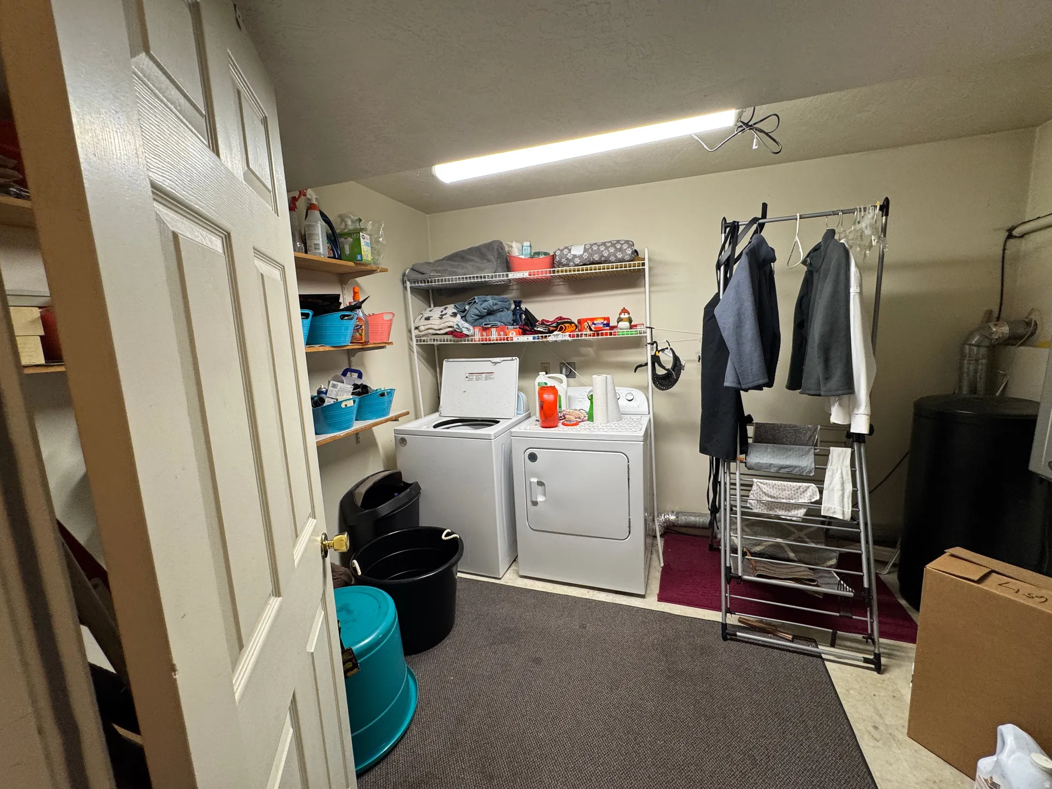 Dedicated laundry area featuring a washer and dryer, wall-mounted shelving, and a dark carpeted floor