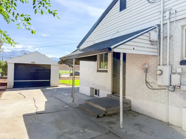 Detached garage with a dark-paneled door, covered side entry, concrete steps, and a concrete driveway