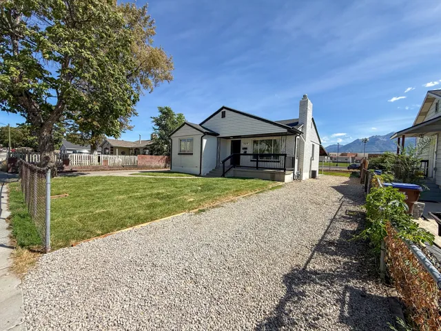 White exterior with black trim, gravel driveway, front lawn, and mature trees