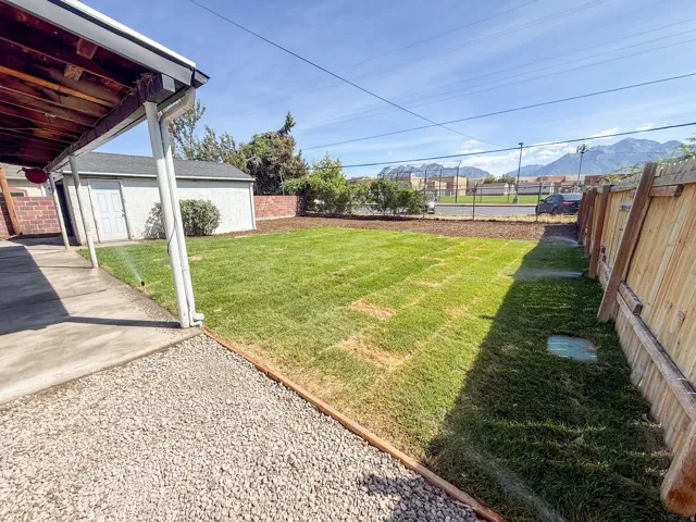 Expansive grass lawn with an irrigation system, wood privacy fencing, and a covered patio area with a concrete surface