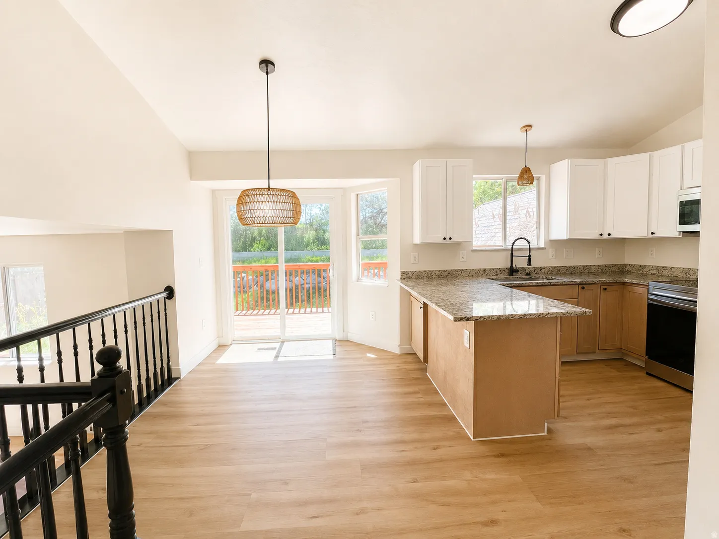 Open-concept kitchen and dining area featuring light wood-finish flooring, a kitchen island with a stone-finish countertop, white upper cabinetry, and a sliding glass door leading to an outdoor deck