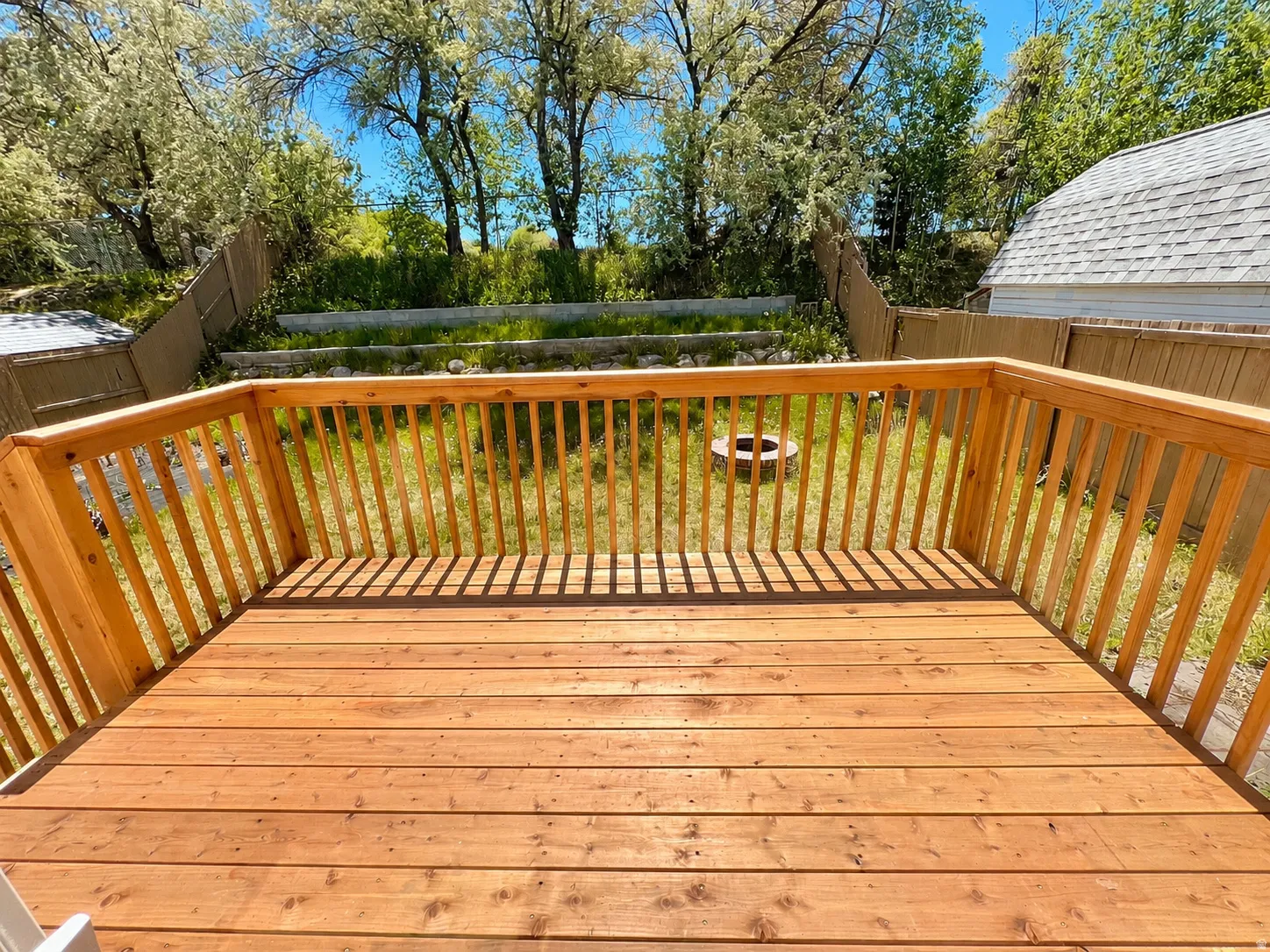 Spacious wood deck with perimeter railing overlooking a tiered backyard with natural landscaping and a fire pit