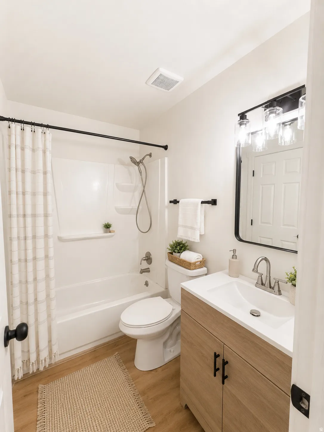 Upstairs bathroom with access from Primary Bedroom featuring a white tub/shower combination, light wood-finish flooring, a contemporary vanity with an integrated sink, and a black-framed mirror--virtually staged.