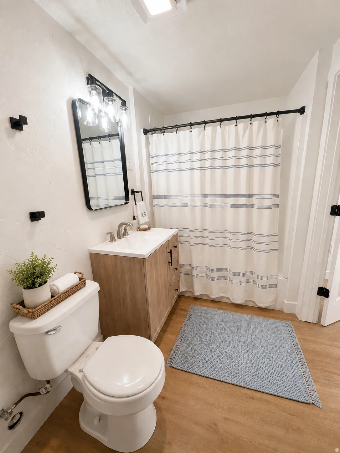Bathroom featuring a light wood-finish vanity with a white countertop and basin, a framed mirror with a three-light fixture, and wood-finish flooring