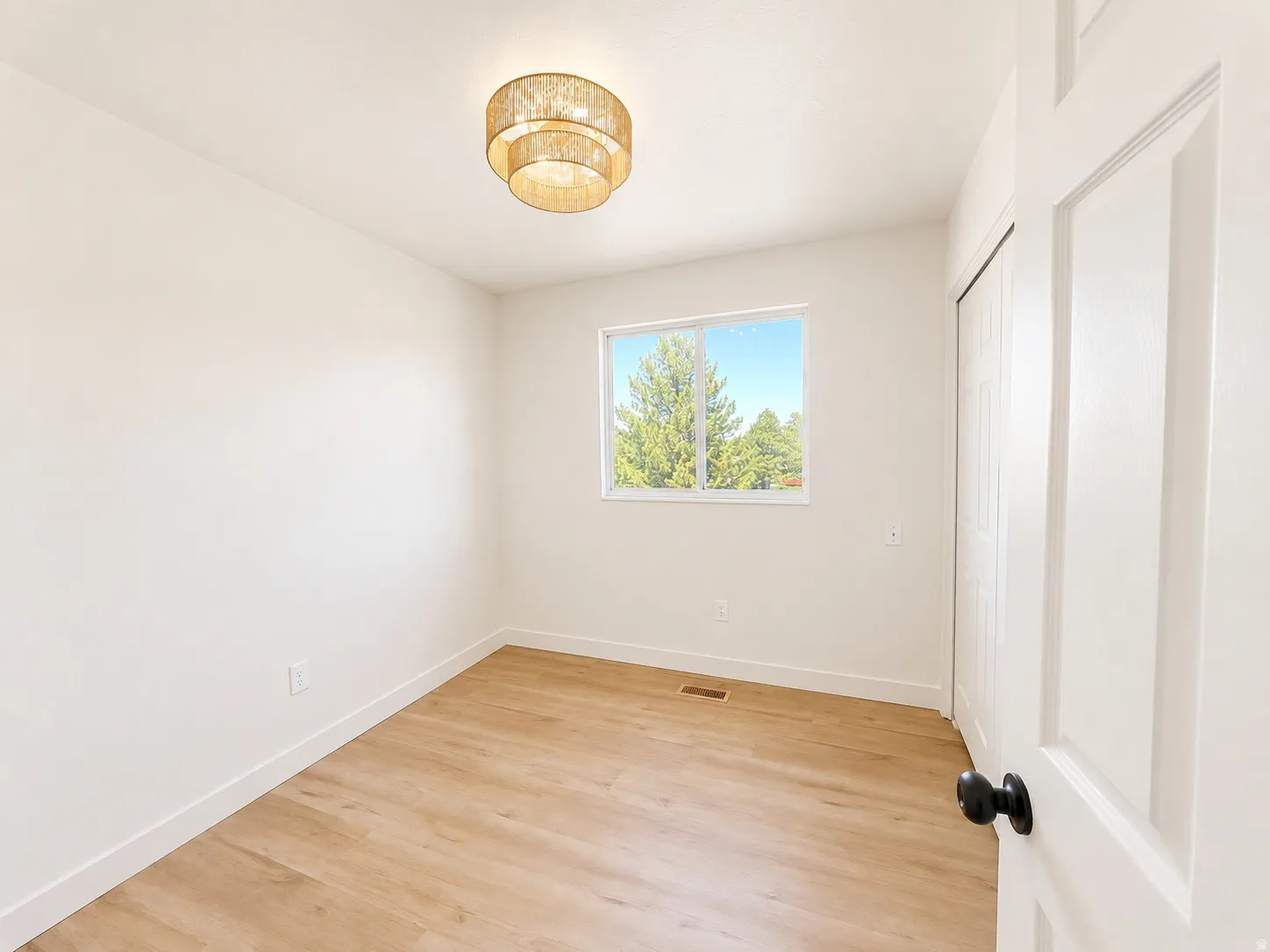 Bedroom 3 featuring a single window, a modern gold-toned ceiling light fixture, wood-finish flooring, white baseboards, and a bi-fold closet door