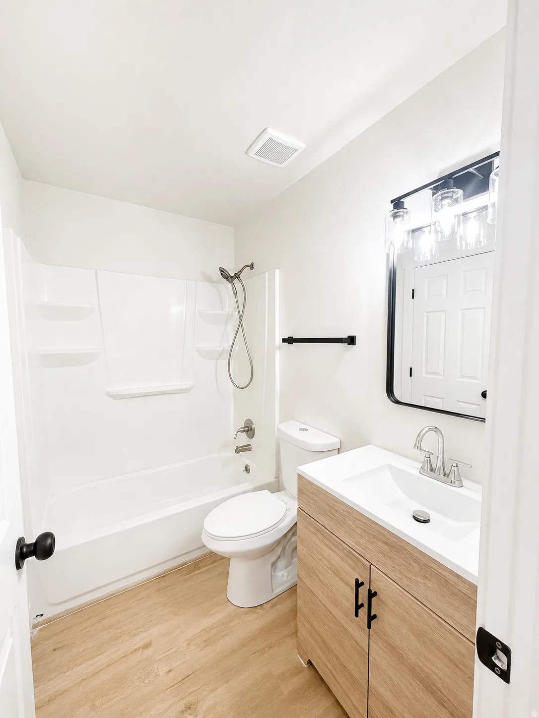 Upstairs bathroom with access from Primary Bedroom featuring a wood-finish vanity with a white countertop and integrated sink, a large framed mirror with overhead lighting, and a white tub/shower combination