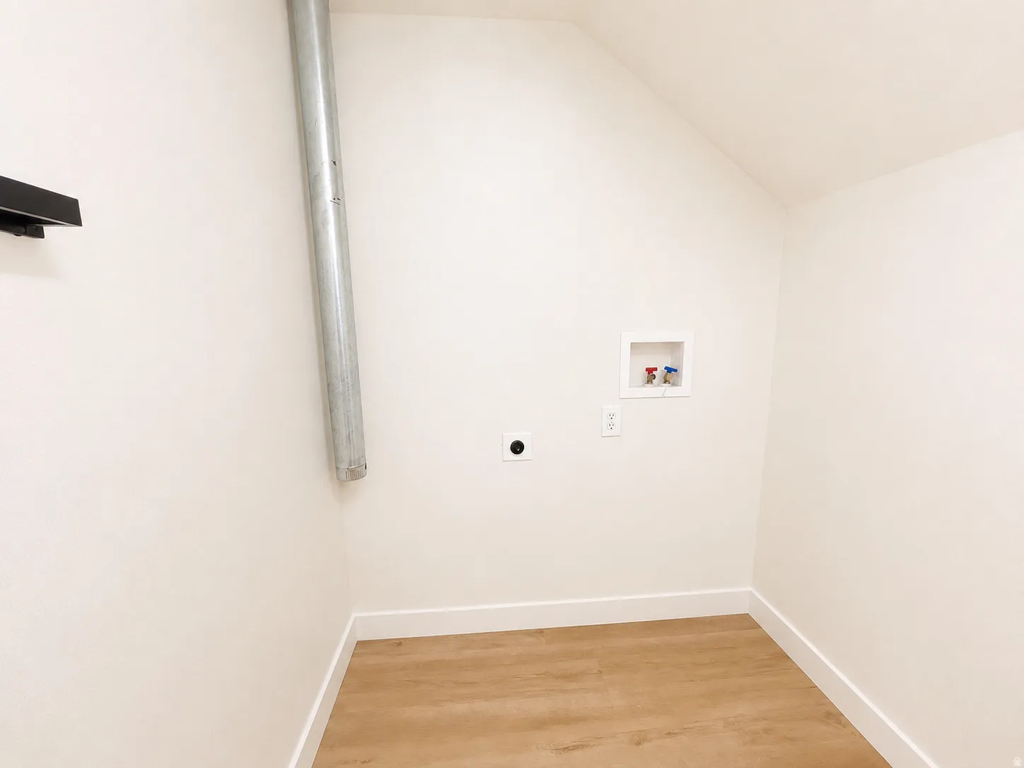 Laundry area featuring wood-finish flooring, white walls, and a sloped ceiling