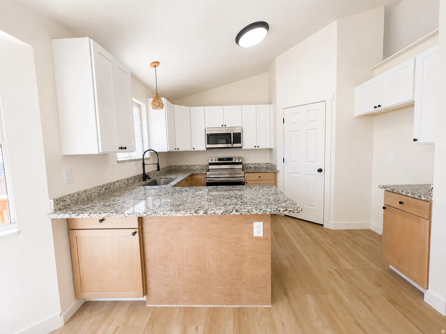 Kitchen featuring wood-finish flooring, white upper cabinetry, light wood lower cabinetry, stainless steel appliances, and speckled countertops