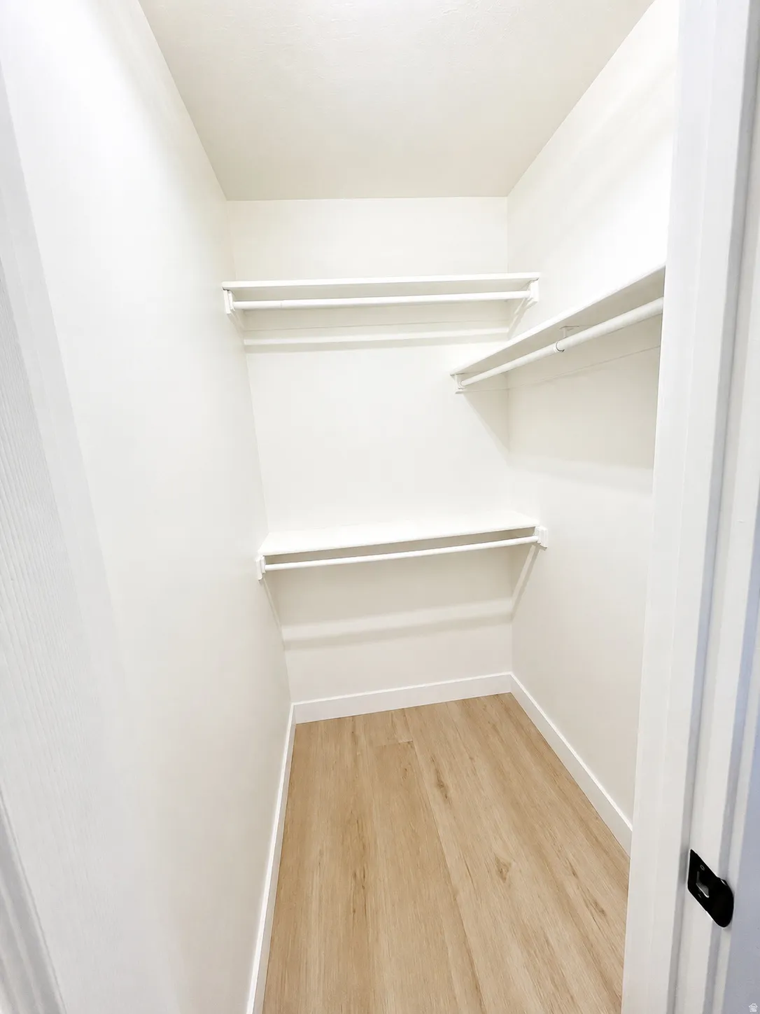 Primary bedroom walk-in closet with integrated shelving, hanging rods, and wood-finish flooring