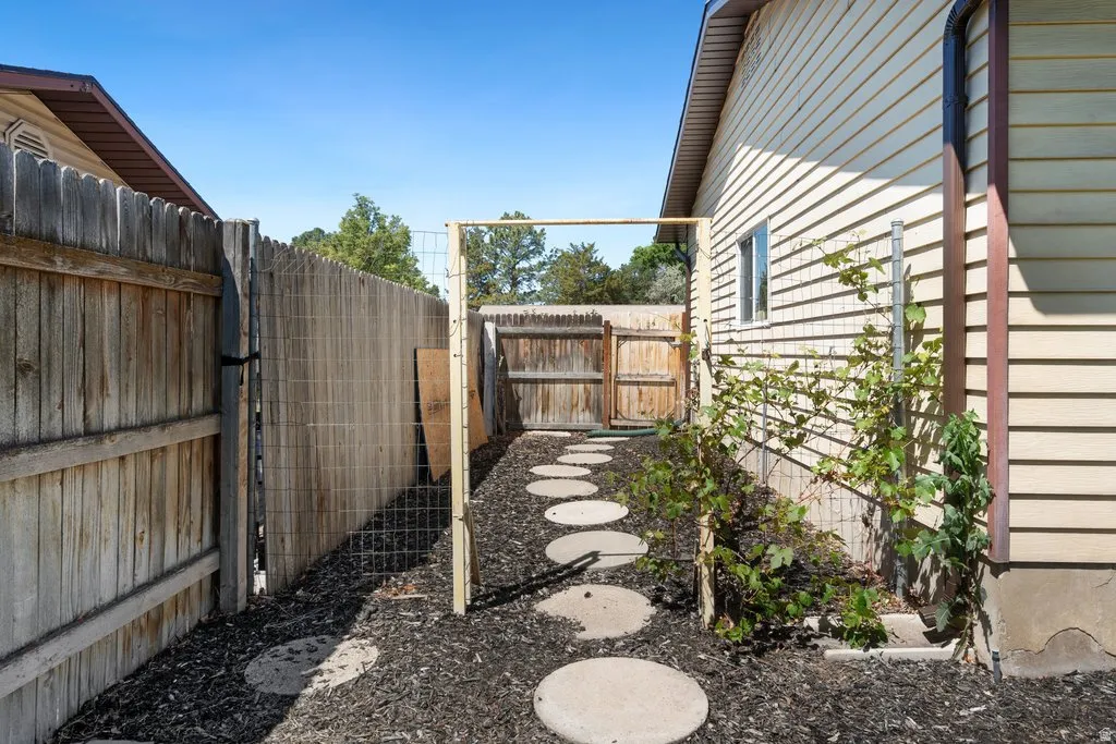 Side yard with a wood picket fence, round stepping stones, and a bark mulch ground cover