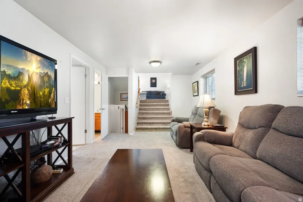 Carpeted lower-level living area with recessed lighting, white walls, and a window featuring blinds