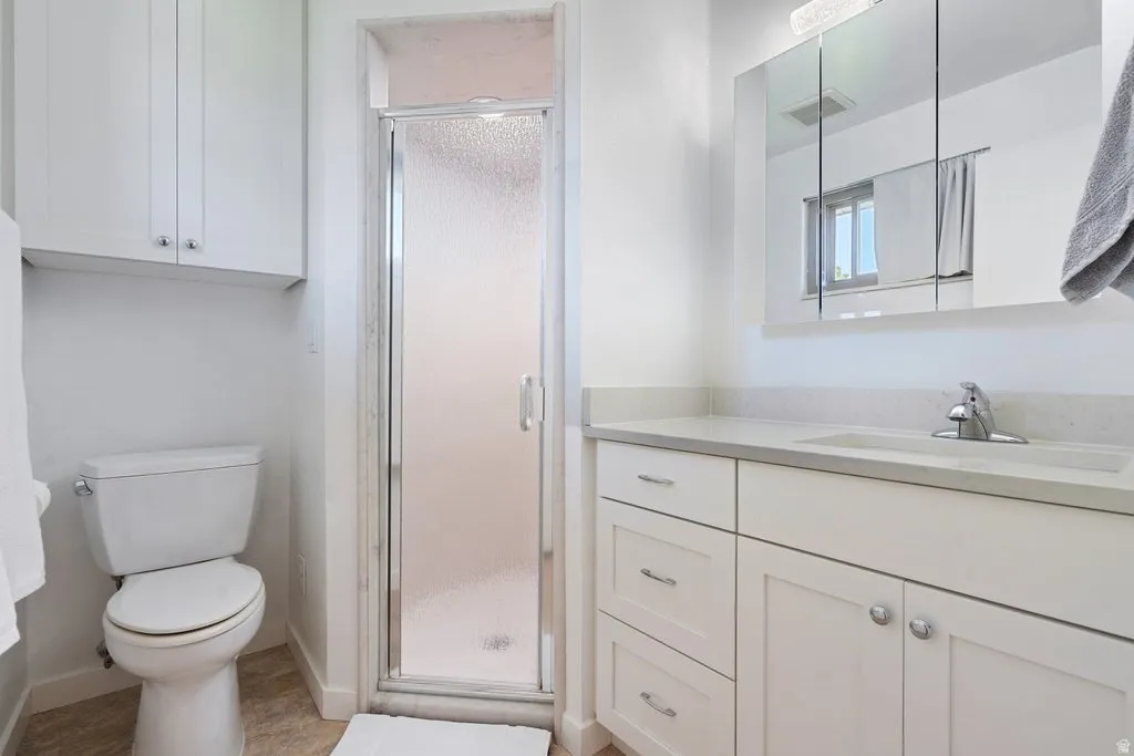 Bathroom featuring a glass-enclosed shower, white vanity with integrated sink, chrome faucet, white cabinetry, and a wall-mounted medicine cabinet