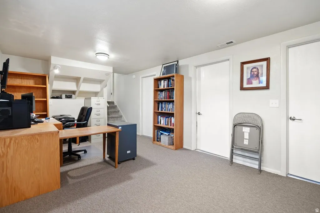 Carpeted lower-level space featuring a recessed staircase, integrated built-in shelving, and multiple white panel doors