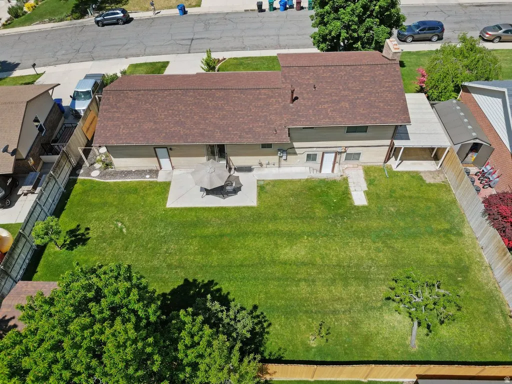 Expansive backyard featuring a large green lawn, concrete patio, and mature trees